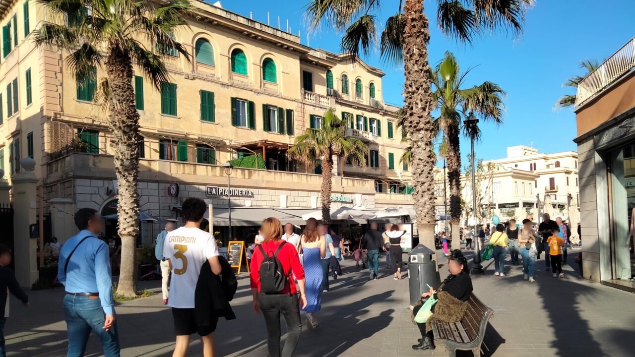 People enjoying the atmosphere of Piazza Anco Marzio in Ostia, surrounded by cafés and historic buildings.