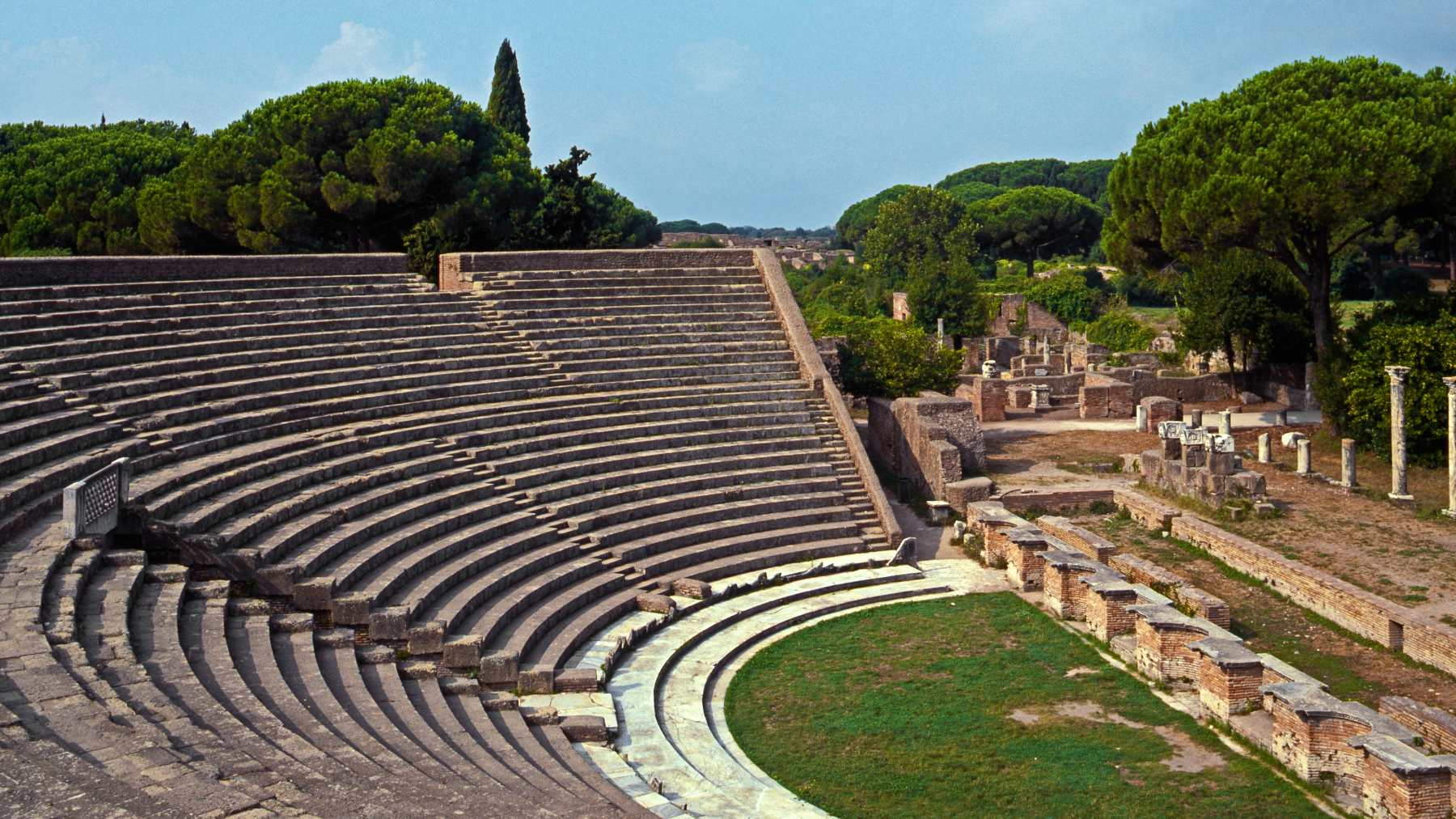 The ancient Roman Theatre at Ostia Antica, with its semicircular stone seating and archaeological surroundings.
